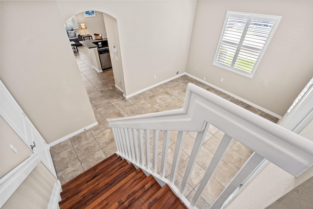 stairs with arched walkways, tile patterned floors, and baseboards