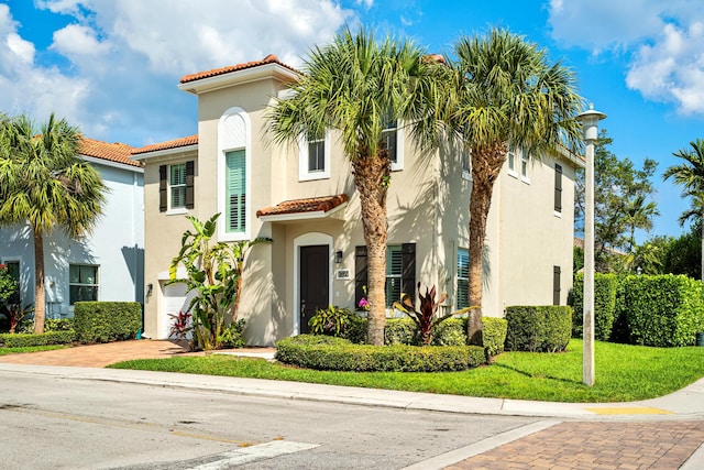 mediterranean / spanish-style home with an attached garage, a tile roof, decorative driveway, stucco siding, and a front lawn