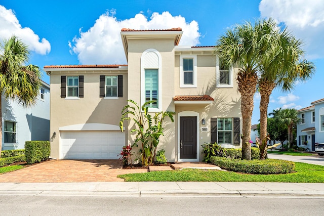 mediterranean / spanish-style home featuring a tiled roof, decorative driveway, an attached garage, and stucco siding