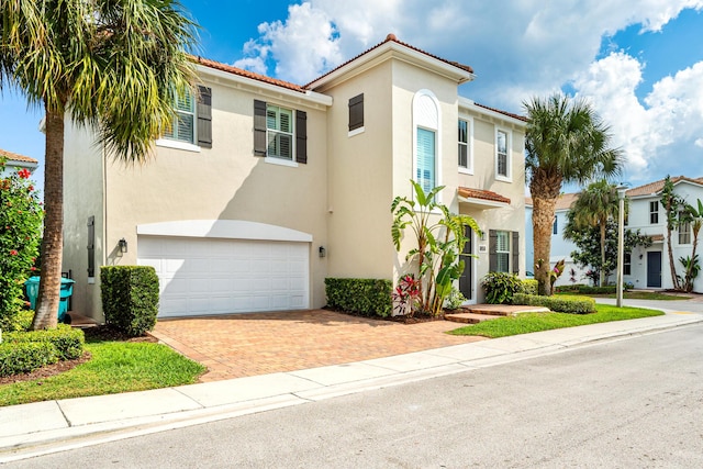 mediterranean / spanish house with an attached garage, a tiled roof, and stucco siding