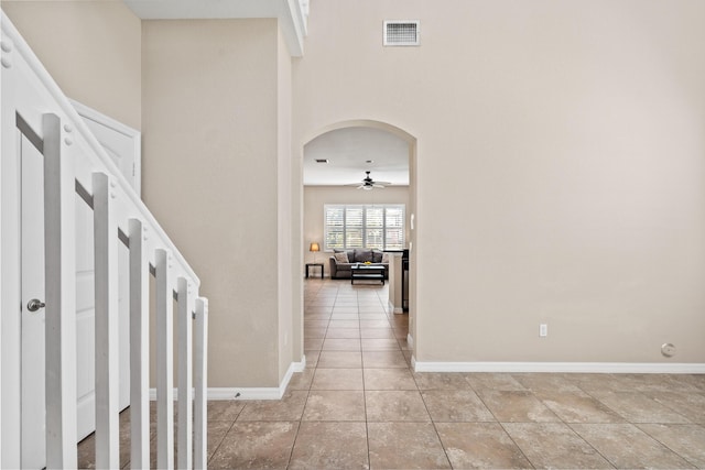 corridor featuring arched walkways, light tile patterned floors, a towering ceiling, visible vents, and baseboards