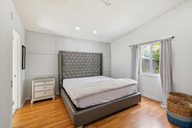 bedroom with lofted ceiling, light hardwood / wood-style flooring, and a textured ceiling