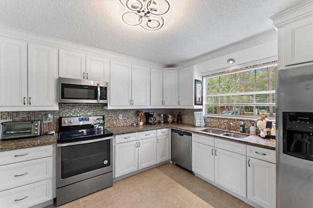 kitchen with white cabinetry, stainless steel appliances, sink, and dark stone countertops