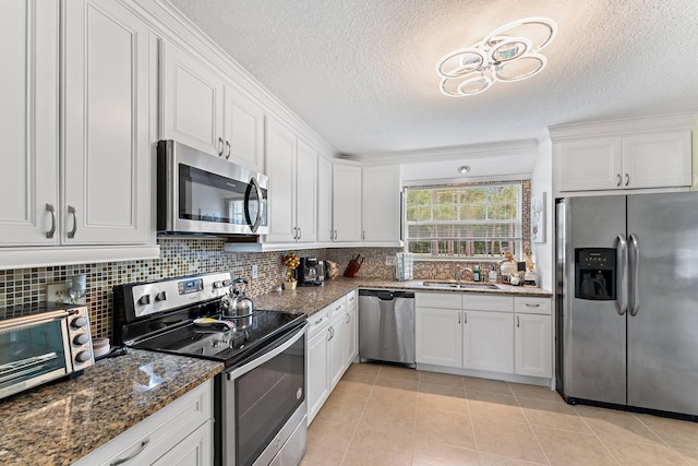 kitchen with sink, appliances with stainless steel finishes, white cabinetry, dark stone countertops, and light tile patterned flooring