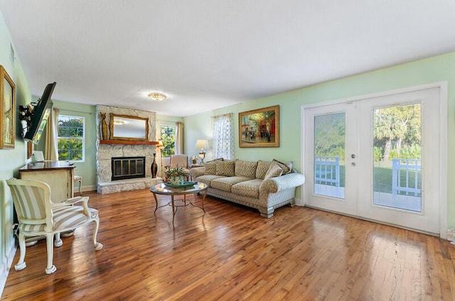 living room with hardwood / wood-style flooring, a wealth of natural light, french doors, and a stone fireplace