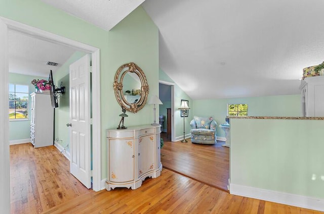 hallway with plenty of natural light, lofted ceiling, and light wood-type flooring