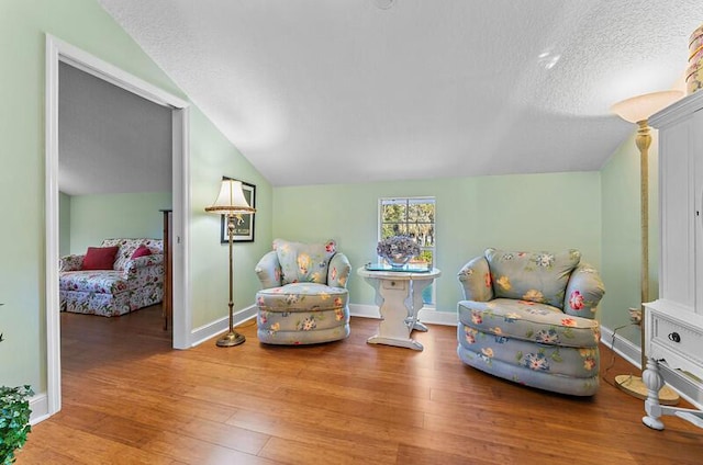 sitting room with lofted ceiling, hardwood / wood-style floors, and a textured ceiling