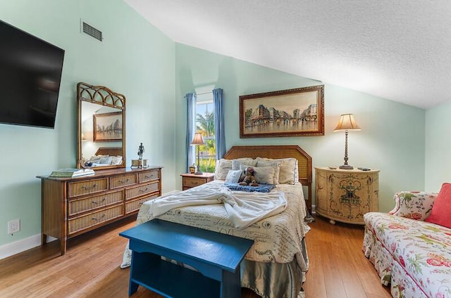 bedroom with lofted ceiling, a textured ceiling, and light wood-type flooring