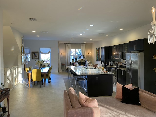 kitchen featuring appliances with stainless steel finishes, an island with sink, a kitchen breakfast bar, sink, and light stone counters