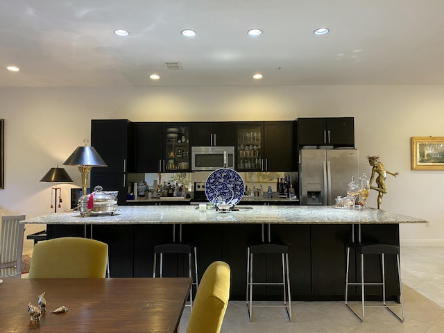 kitchen featuring light tile patterned floors, a kitchen bar, stainless steel appliances, and a large island