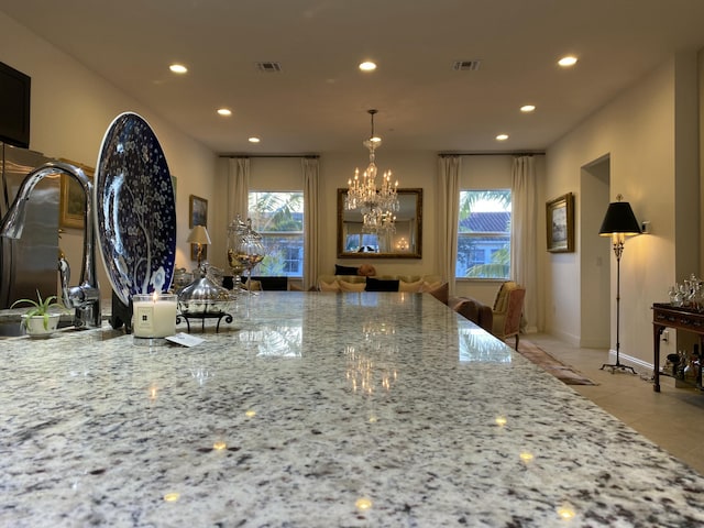 kitchen with a notable chandelier, light tile patterned floors, pendant lighting, and light stone countertops