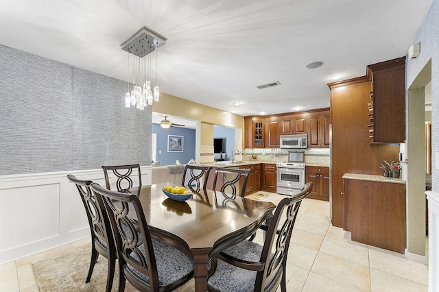 dining space featuring visible vents, a ceiling fan, a wainscoted wall, a decorative wall, and light tile patterned flooring