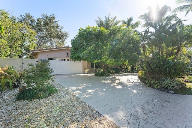 view of front facade with a tile roof, stucco siding, fence, a garage, and driveway