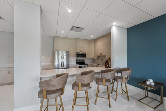 kitchen featuring kitchen peninsula, light brown cabinetry, stainless steel appliances, and a breakfast bar area