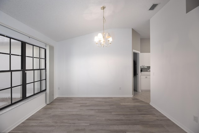 unfurnished dining area featuring a textured ceiling, light hardwood / wood-style floors, an inviting chandelier, and lofted ceiling