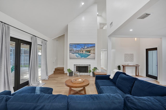 living room featuring french doors, a fireplace, high vaulted ceiling, and light hardwood / wood-style flooring