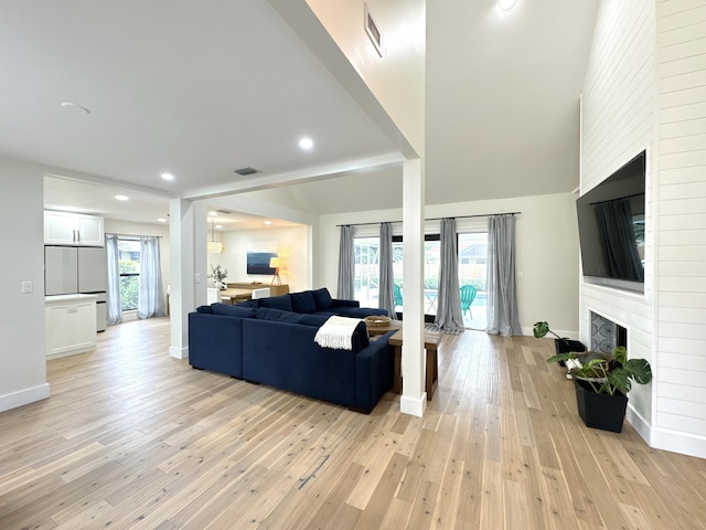 living room featuring lofted ceiling, a large fireplace, and light hardwood / wood-style flooring