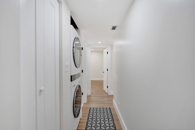 laundry room featuring stacked washer and dryer and light hardwood / wood-style flooring