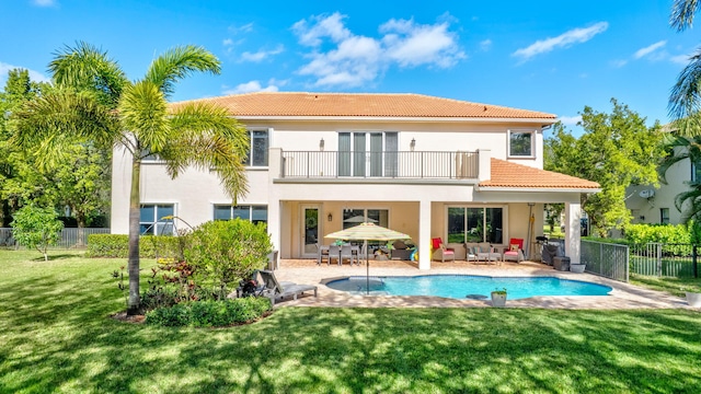 rear view of property featuring a fenced in pool, a balcony, a yard, and a patio area