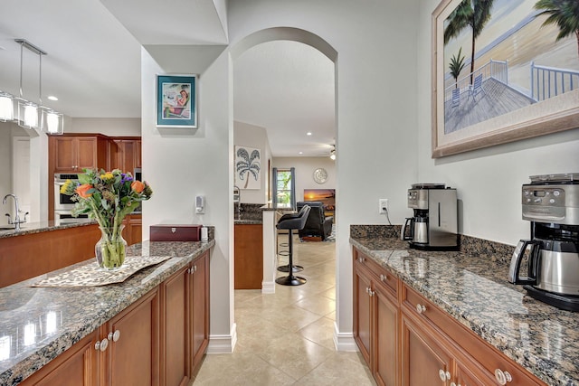 kitchen with pendant lighting, sink, dark stone countertops, ceiling fan, and stainless steel double oven