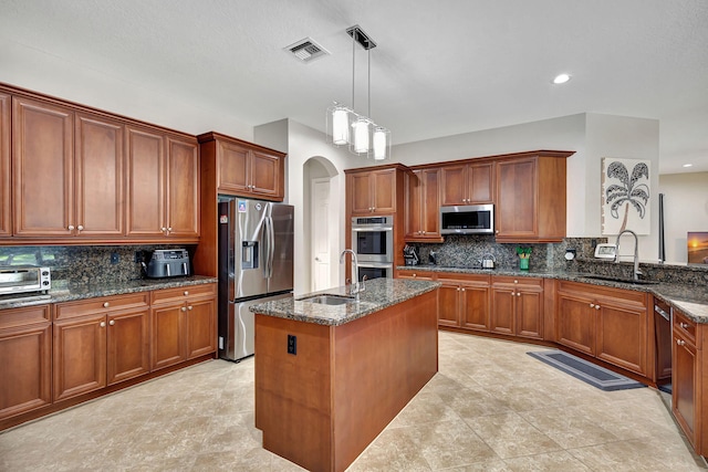 kitchen featuring sink, decorative light fixtures, stainless steel appliances, and a center island with sink