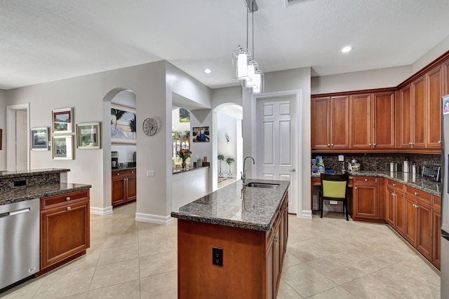 kitchen with dishwasher, a kitchen island with sink, dark stone countertops, light tile patterned flooring, and decorative light fixtures