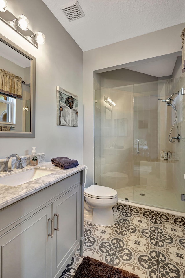 bathroom featuring toilet, a textured ceiling, vanity, a shower with door, and tile patterned flooring