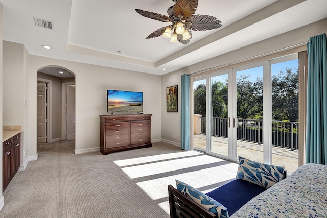 bedroom featuring ceiling fan, access to exterior, a tray ceiling, light carpet, and french doors