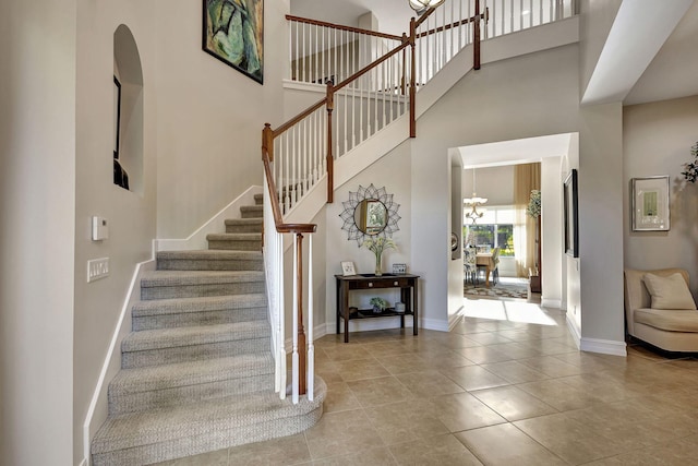 staircase with tile patterned flooring, a towering ceiling, and an inviting chandelier