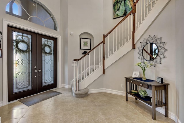 foyer with a high ceiling, light tile patterned flooring, a wealth of natural light, and french doors