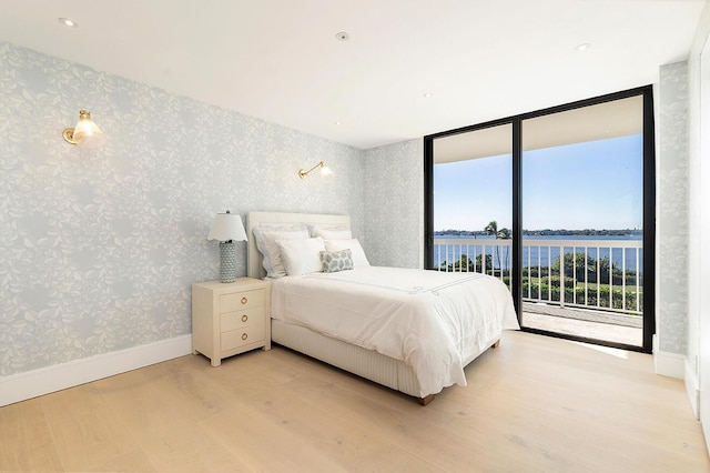 bedroom with access to exterior, multiple windows, a wall of windows, and a water view