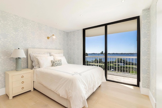 bedroom with multiple windows, a wall of windows, access to outside, and a water view