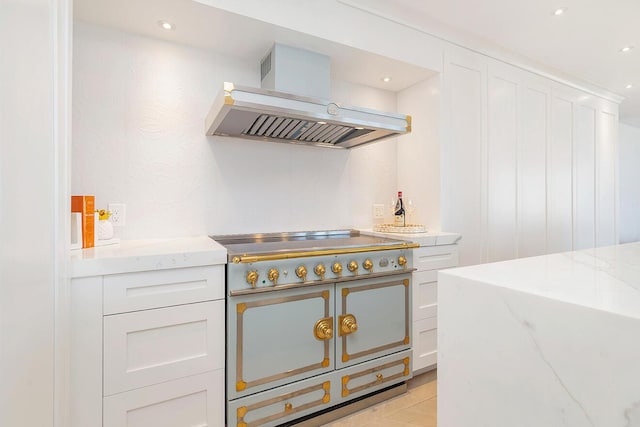 kitchen featuring stainless steel gas stovetop, white cabinetry, island exhaust hood, light stone countertops, and range with two ovens