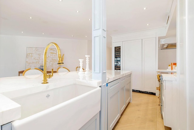 kitchen featuring light stone countertops, white cabinetry, sink, and custom range hood