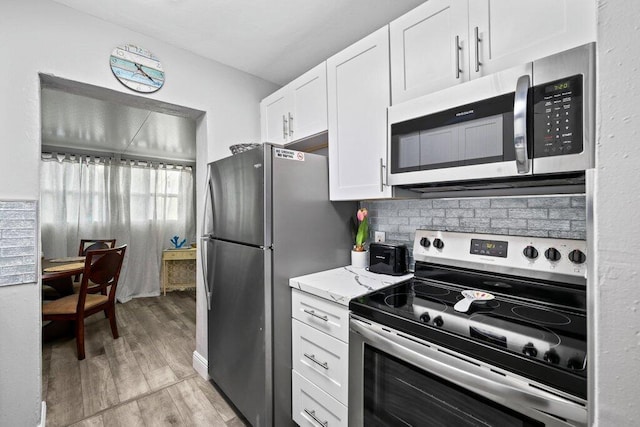 kitchen featuring appliances with stainless steel finishes, backsplash, light stone counters, white cabinets, and light wood-type flooring