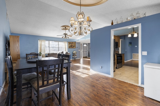 dining area with ceiling fan with notable chandelier, a textured ceiling, hardwood / wood-style flooring, and a tray ceiling