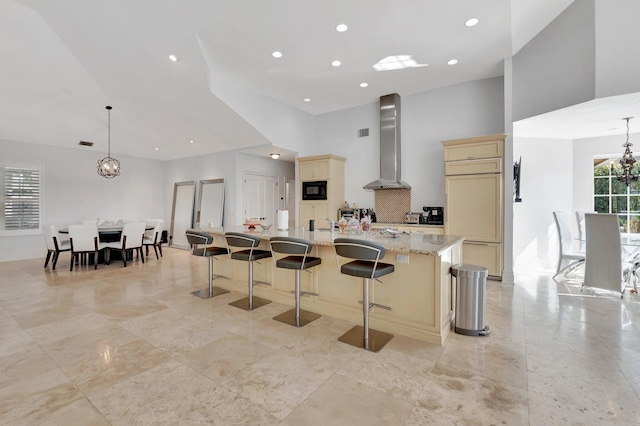 kitchen with light stone countertops, pendant lighting, a large island with sink, wall chimney range hood, and built in appliances