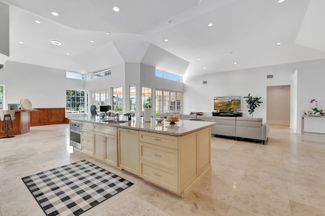 kitchen featuring a kitchen island with sink, oven, light stone counters, cream cabinets, and sink