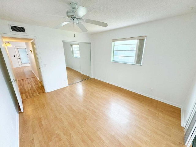 unfurnished bedroom with a textured ceiling, light wood-type flooring, a closet, and ceiling fan