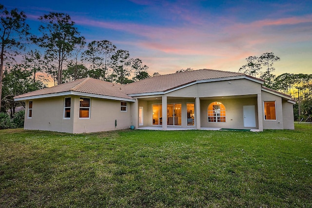 back house at dusk featuring a lawn and a patio area