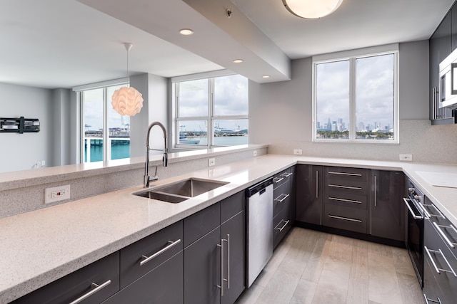 kitchen featuring a wealth of natural light, sink, stainless steel dishwasher, pendant lighting, and a water view