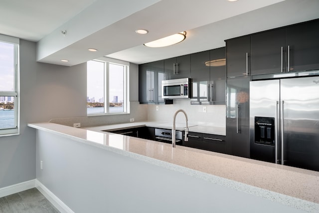 kitchen with backsplash, light hardwood / wood-style flooring, light stone countertops, kitchen peninsula, and stainless steel appliances