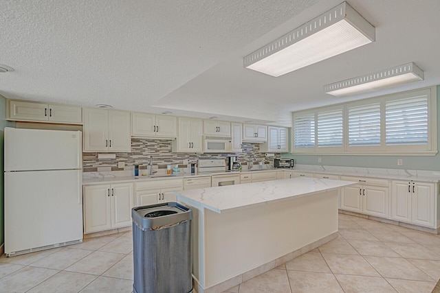 kitchen featuring sink, a kitchen island, light tile patterned flooring, and white appliances