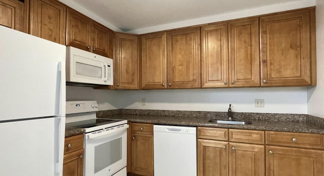 kitchen featuring white appliances, dark stone counters, and sink