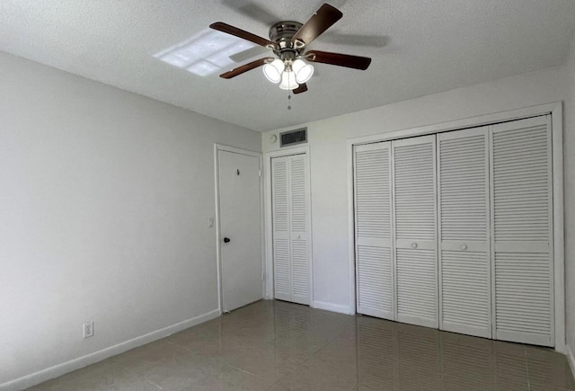 unfurnished bedroom with tile patterned floors, ceiling fan, a textured ceiling, and multiple closets