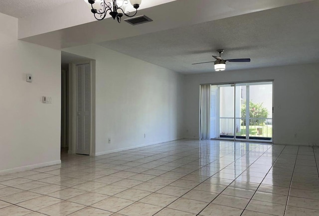 tiled empty room featuring ceiling fan with notable chandelier and a textured ceiling