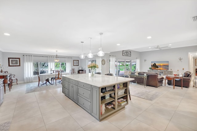 kitchen with light tile patterned flooring, light stone countertops, gray cabinetry, a center island, and decorative light fixtures