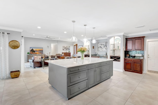 kitchen with gray cabinetry, a kitchen island, open floor plan, ornamental molding, and pendant lighting