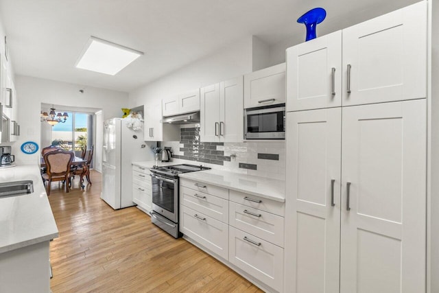 kitchen featuring white cabinetry, tasteful backsplash, light hardwood / wood-style flooring, a notable chandelier, and stainless steel appliances