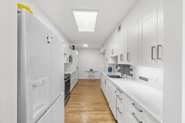 kitchen with sink, white cabinetry, tasteful backsplash, light wood-type flooring, and white appliances